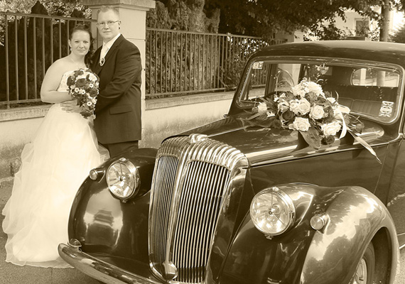 Das Brautpaar mit dem Hochzeits-Oldtimer in Sepia-Färbung.